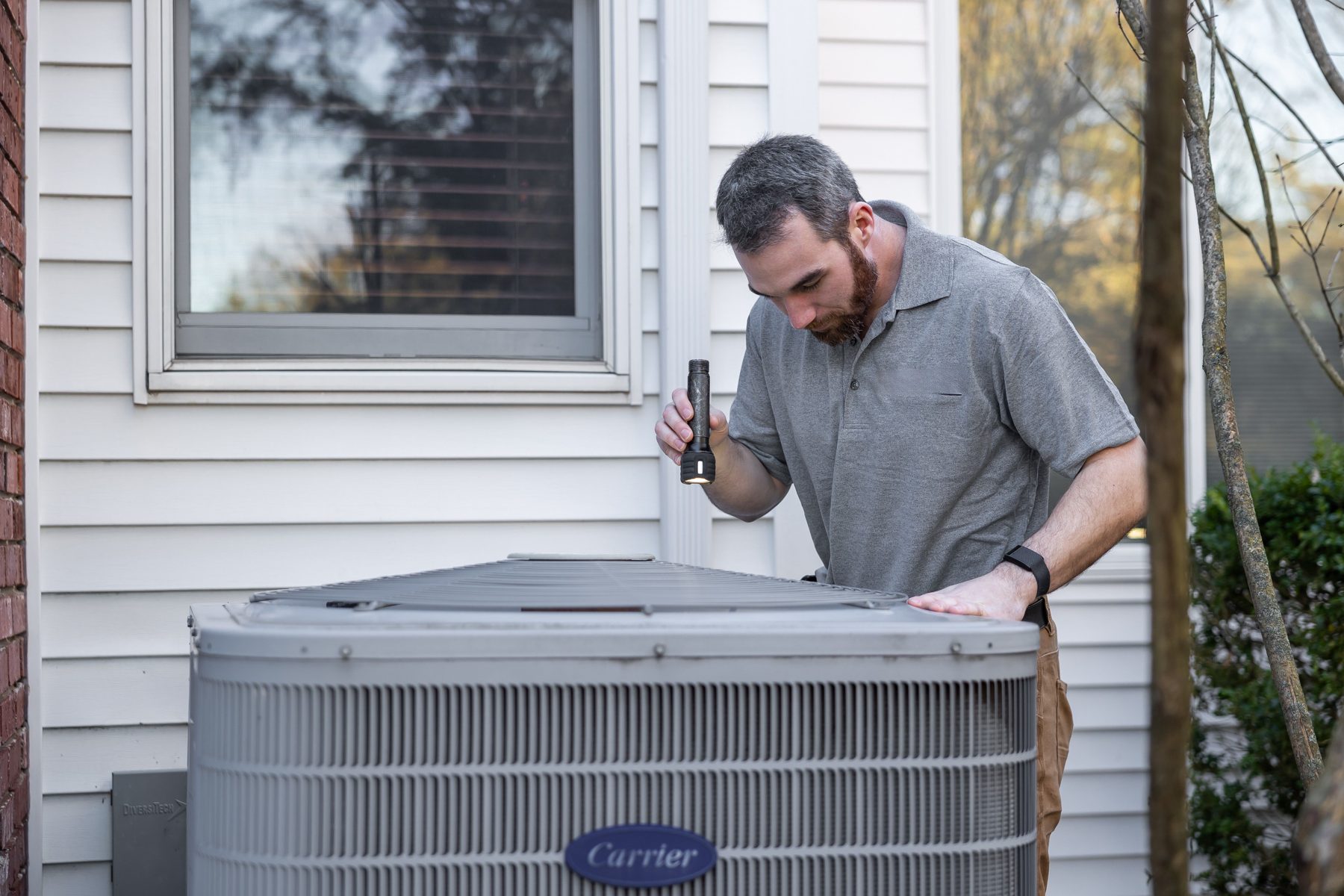 HVAC technician inspecting an outdoor condenser beside a house